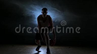 一个年轻的成年人，篮球运动员运球，黑暗的室内篮球场。 慢动作